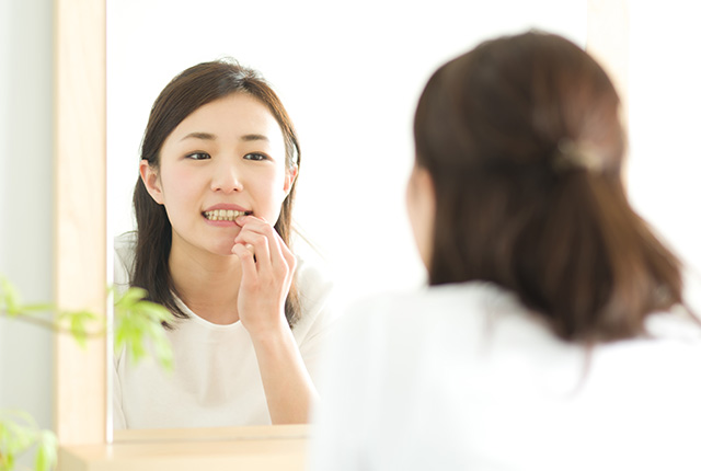 鏡で口元を見る女性